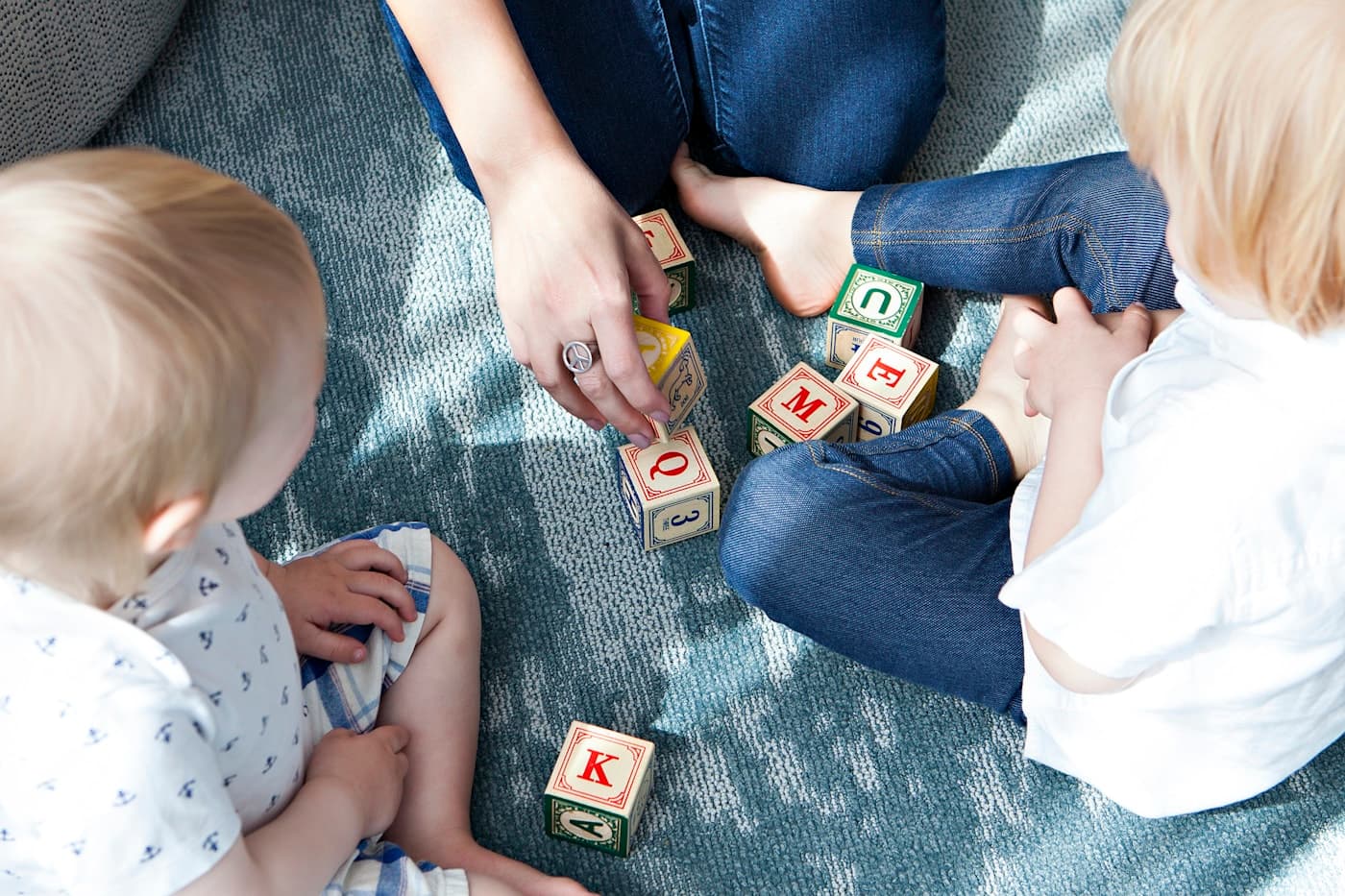 Two young children playing with wooden blocks on a rug.